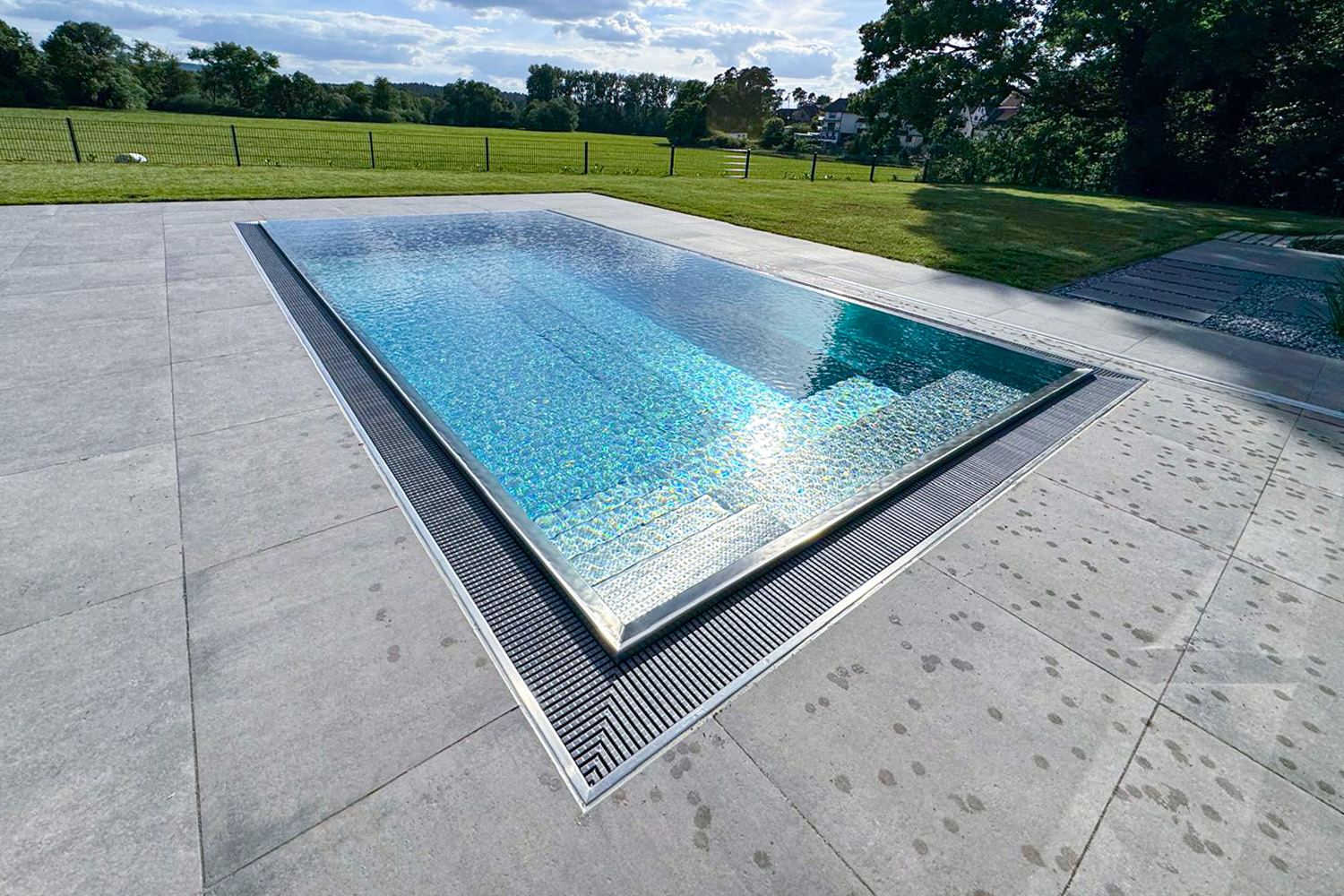 Edelstahlpool mit Sitzbank und Ausblick auf Grünfläche Überlaufpool aus Edelstahl mit eingelassener Treppe und weitläufigem Garten