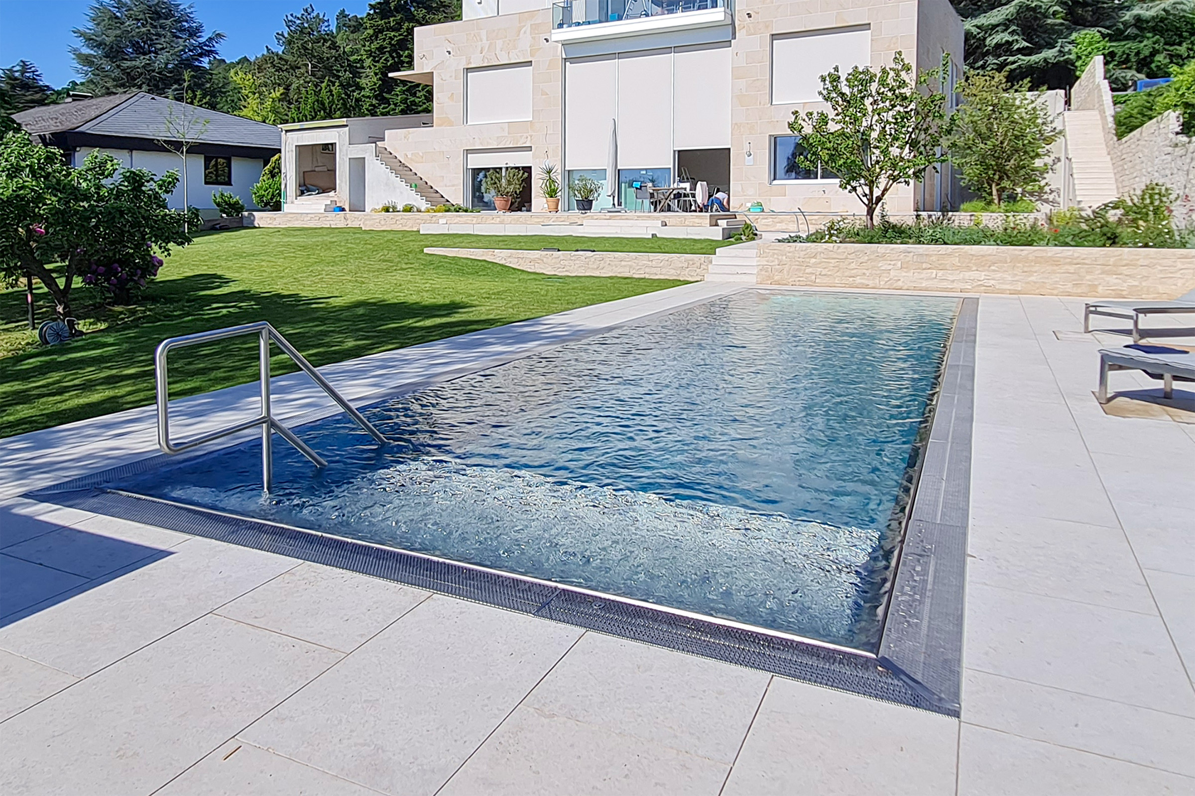 Moderner Edelstahlpool mit Treppenzugang und Wasser in Bewegung Edelstahlpool mit aktiver Wasserbewegung an der Luftsprudelliege, eingebettet in eine gepflegte Rasen- und Gartenanlage