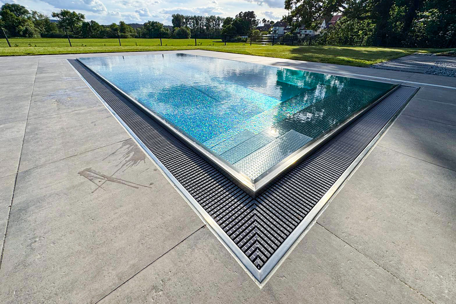 Edelstahl-Überlaufbecken mit glasklarer Wasseroberfläche und rutschhemmendem Boden Blick auf den Überlauf-Edelstahlpool mit genoppter Bodenfläche und Wasserlinie auf Beckenrandhöhe