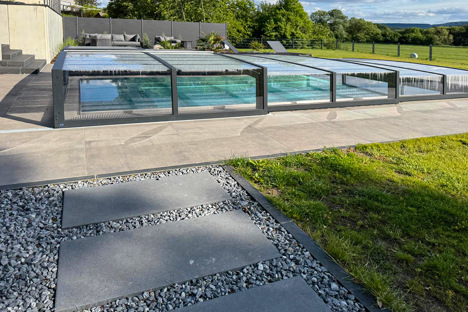Flache Poolüberdachung in RAL 7021 über Edelstahlbecken mit Sitzbereich Edelstahlbecken mit transluzenter Poolüberdachung und Blick auf moderne Terrasse