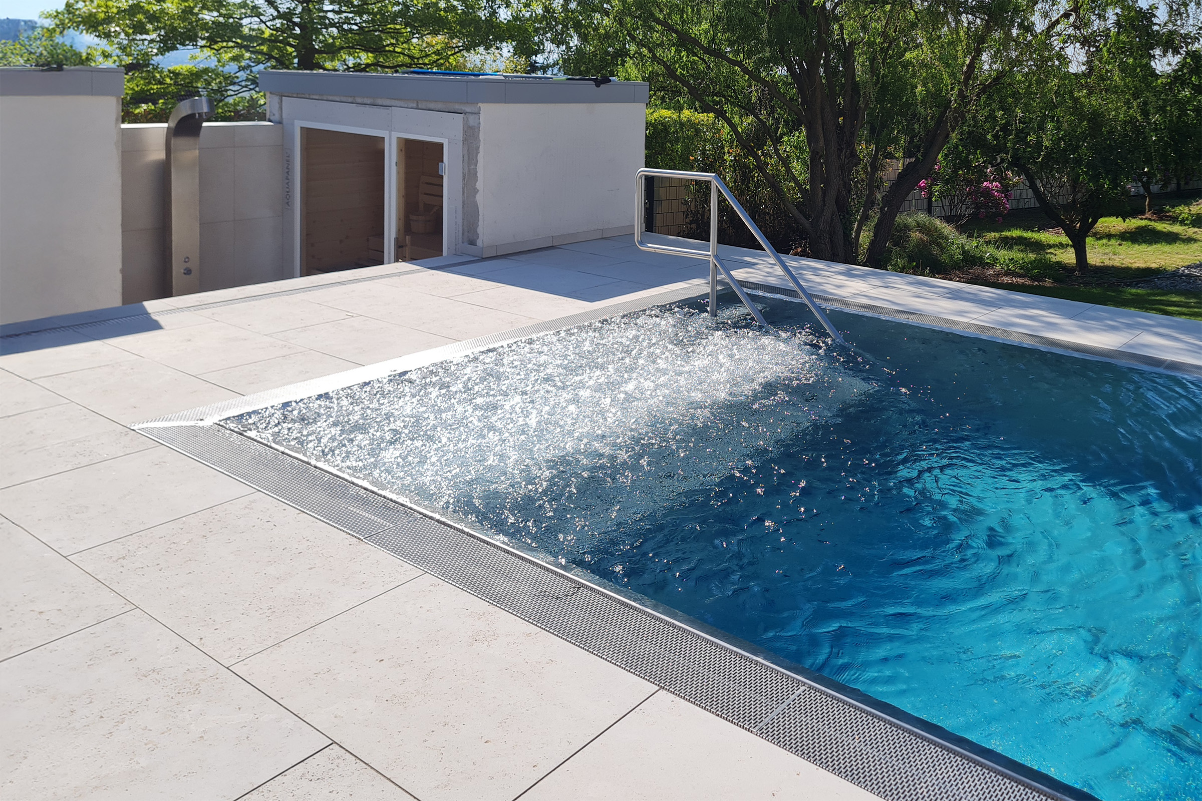 Edelstahlpool mit aktiver Luftsprudelliege und modernem Treppenzugang Edelstahl-Überlaufbecken mit eingeschalteter Luftsprudelliege, Treppeneinstieg mit Handlauf und Blick auf die Sauna im Hintergrund