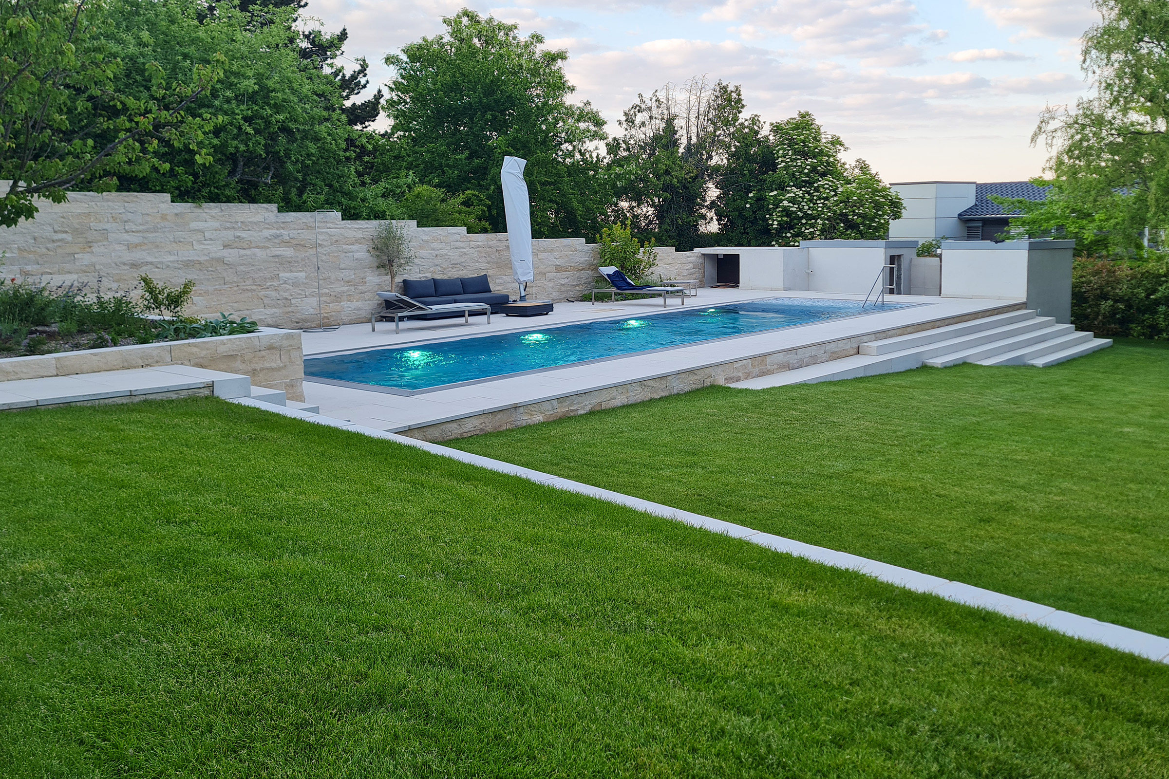 Edelstahlschwimmbecken mit grüner LED-Beleuchtung am Abend Edelstahlpool mit eingeschalteter LED-Beleuchtung bei Dämmerung, eingebettet in modern gestaltete Gartenanlage