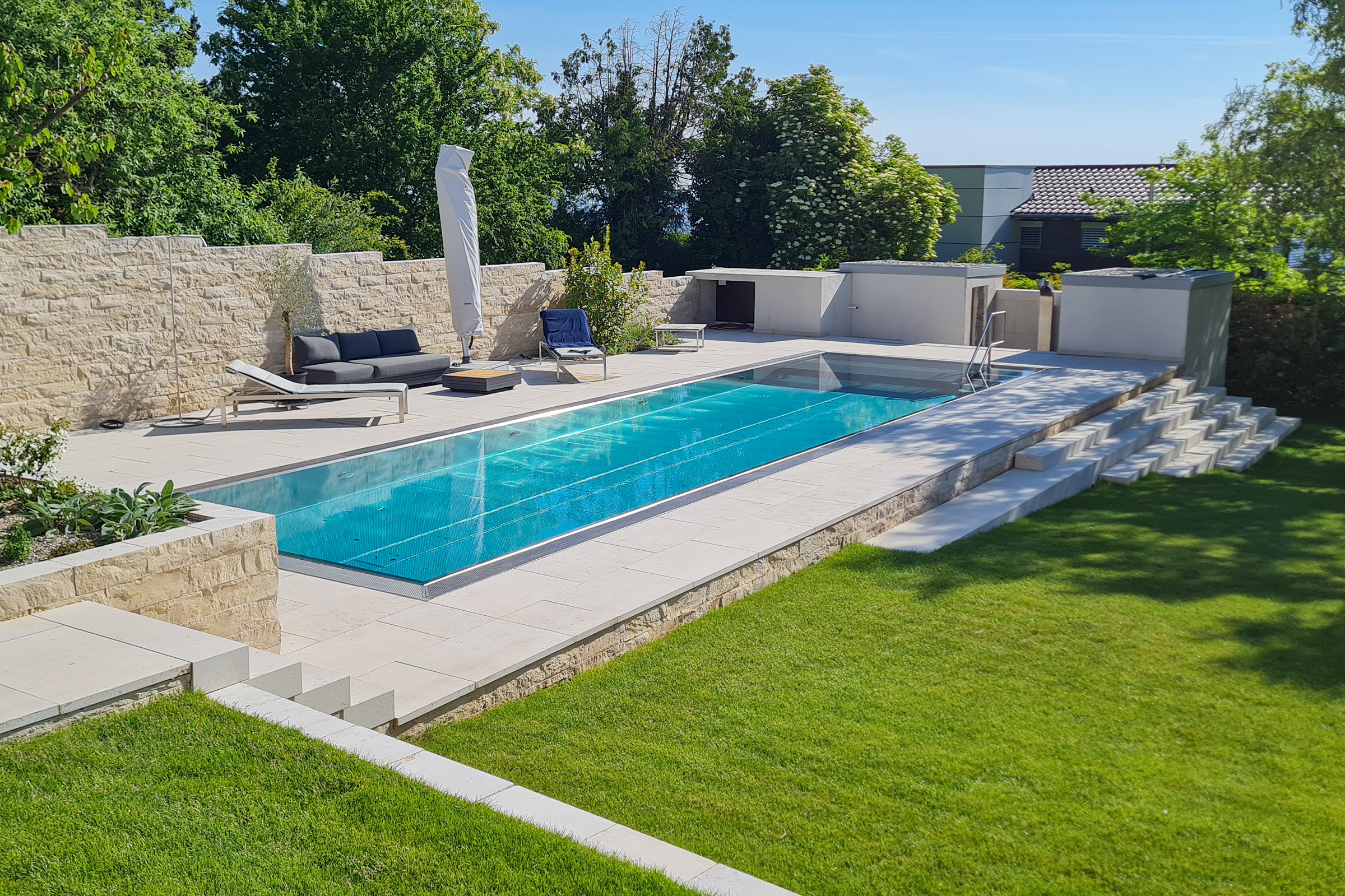 Edelstahl-Überlaufpool mit geschlossener Rollladenabdeckung Edelstahlpool mit flacher Unterflurabdeckung aus Polycarbonatlamellen und modernem Außenbereich
