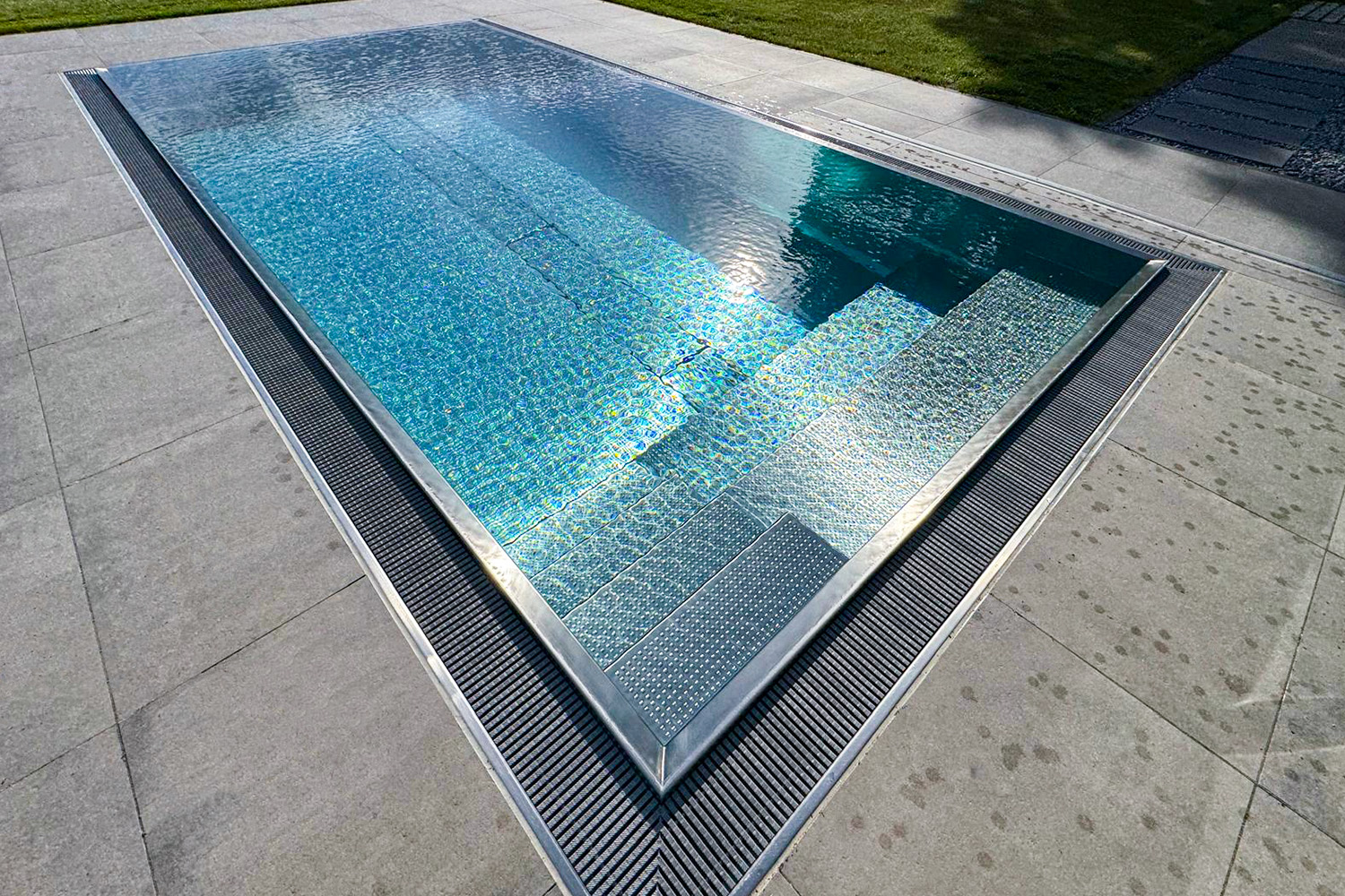 Edelstahlpool mit glatter Wasseroberfläche und eingebauter Sitzbank Frontalansicht des Edelstahlpools mit integrierter Sitzbank und glatter Wasserfläche
